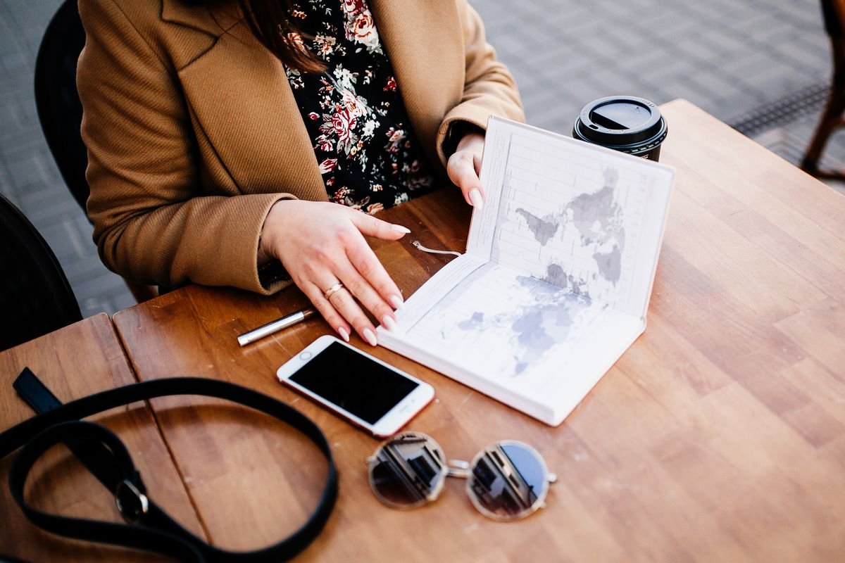 Voyageuse consultant un carnet de voyage, un smartphone et un café à une table pour gérer sa réservation Airbnb