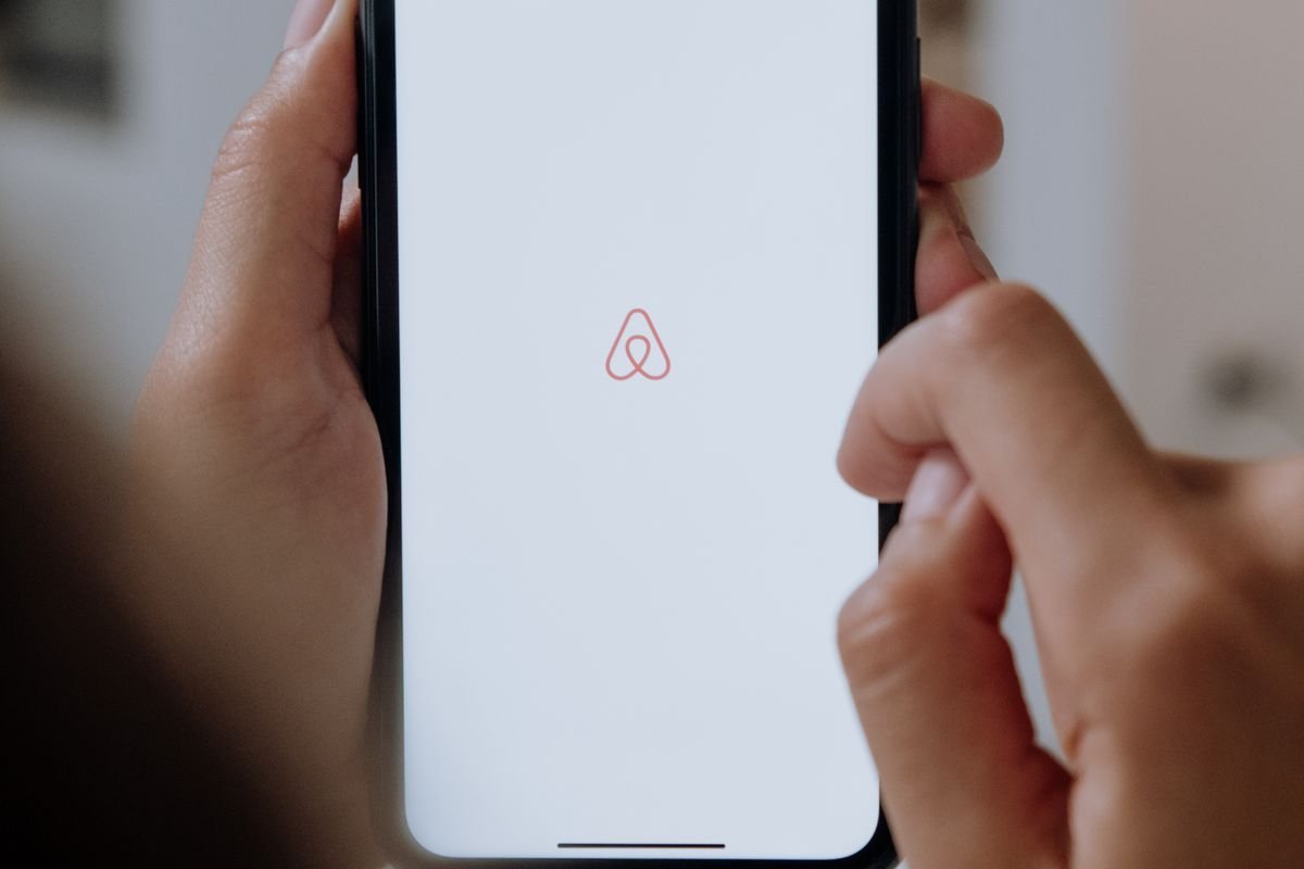 Mains tenant un smartphone affichant le logo Airbnb pour annuler une réservation depuis l'application