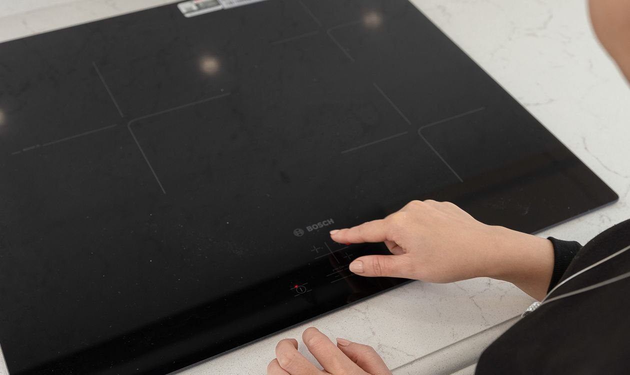 Doigt posé sur le bandeau de commandes tactile d'une plaque à induction pour sélectionner une zone