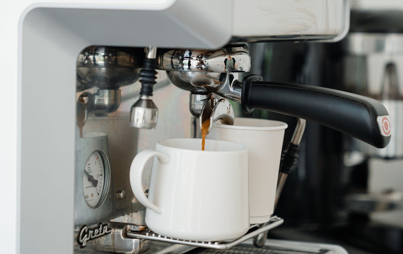 Café qui s'écoule normalement du groupe d'une machine à expresso dans une tasse blanche