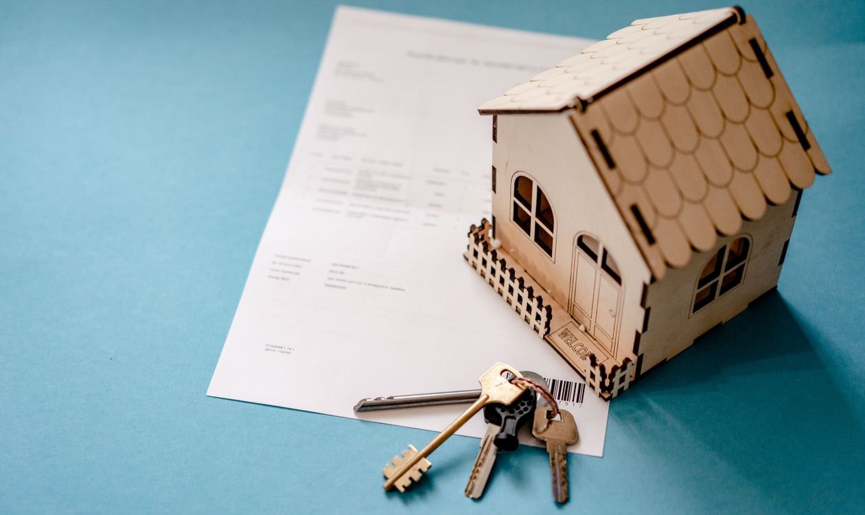 Maison miniature en bois posée sur un document administratif avec un trousseau de clés, symbole de fiscalité immobilière