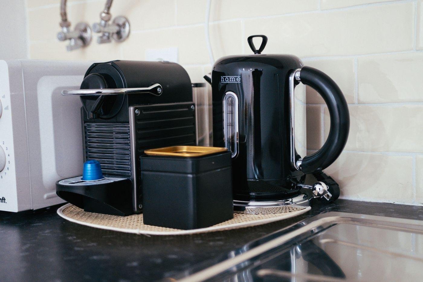 Machine à café à capsules et bouilloire posées sur le plan de travail d'une cuisine de logement loué