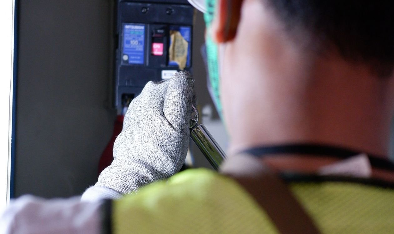 Main qui coupe un disjoncteur au tableau électrique pour réinitialiser une plaque à induction défaillante