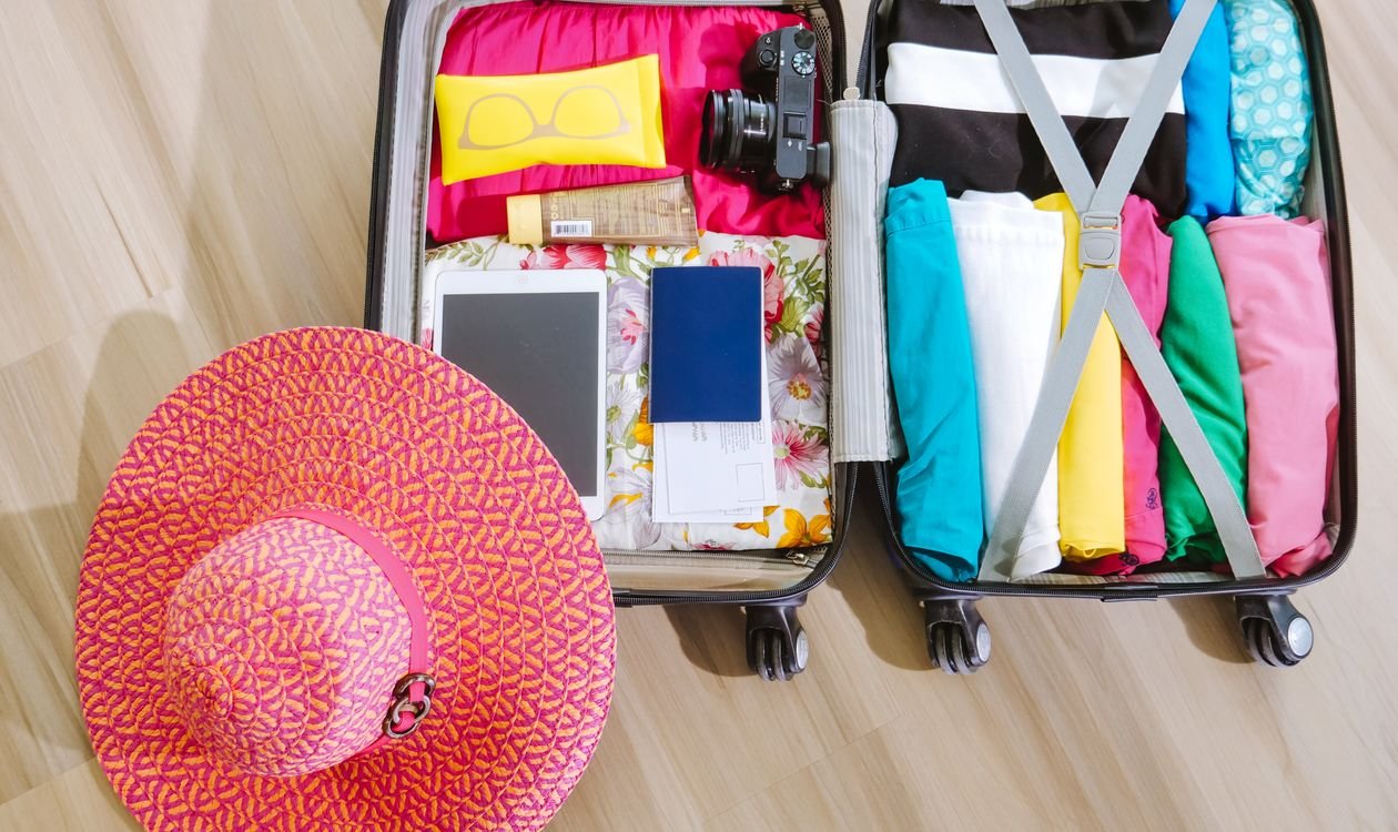 Valise ouverte avec appareil photo, chapeau et lunettes de soleil, illustrant la saisonnalité touristique