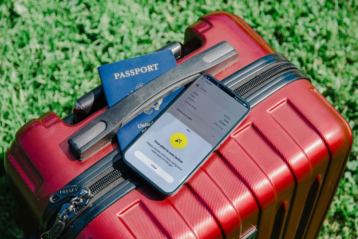 Valise de voyage, passeport et smartphone posés sur l'herbe, symbolisant un séjour annulé pour force majeure